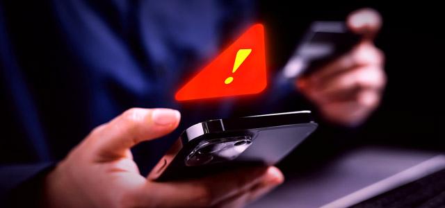 A person holding a smartphone and credit card with a glowing red warning symbol above the phone.